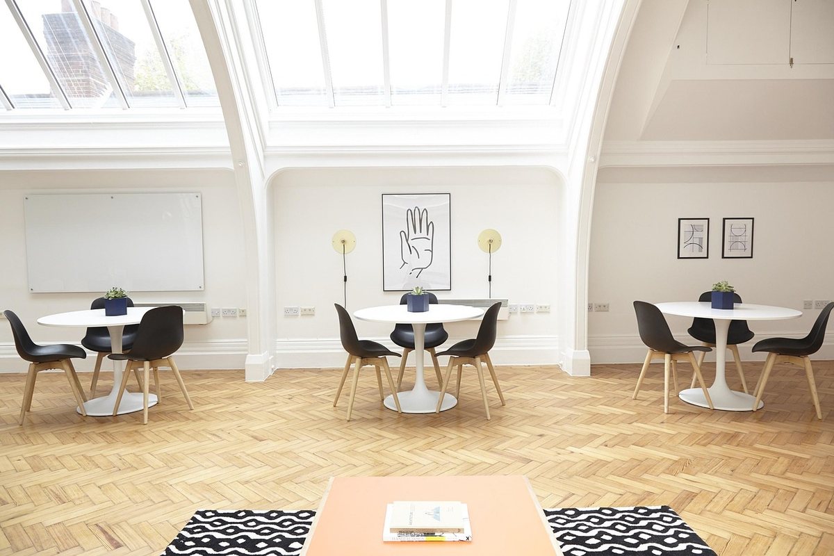 Three small round tables with moulded armless chairs in a white attic room.