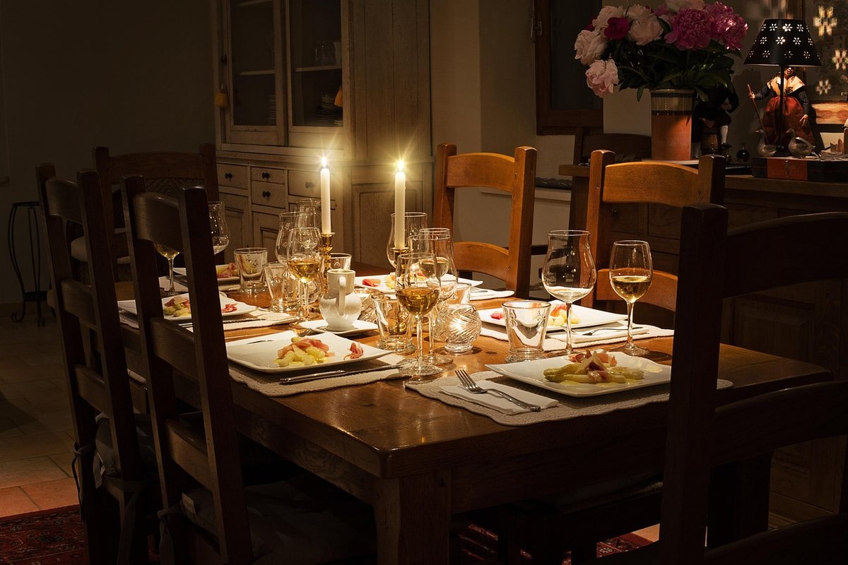 A candlelit dinner table laid for six, with dark wooden dining chairs pulled in.