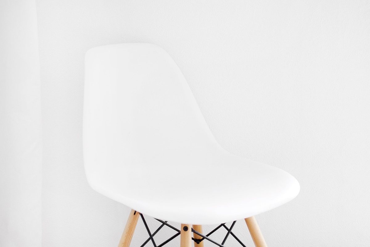 A single white moulded dining chair with wooden legs against a plain white wall.