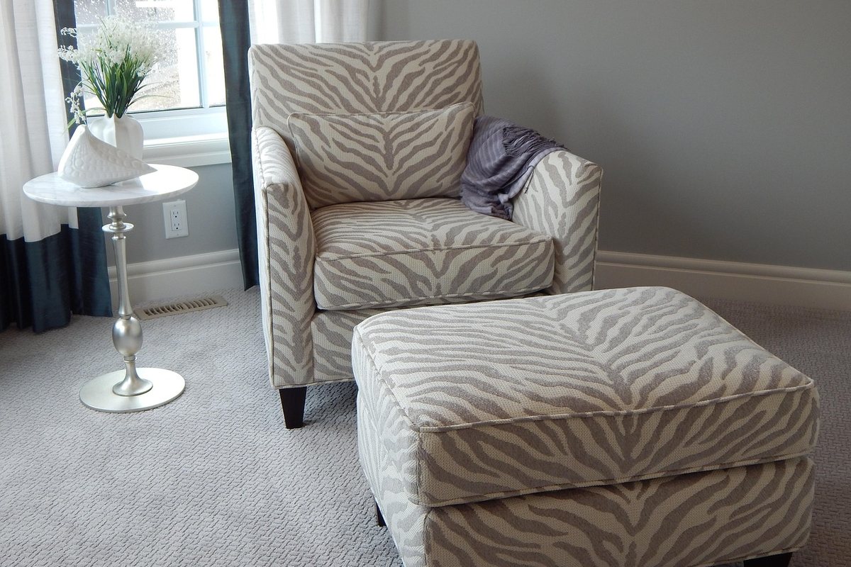 A patterned armchair with a matching ottoman in front of it beside a window.