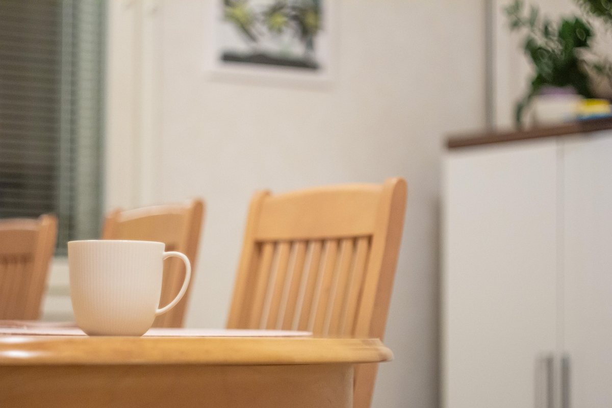 A mug on a wooden table with the slatted back of a dining chair behind it.