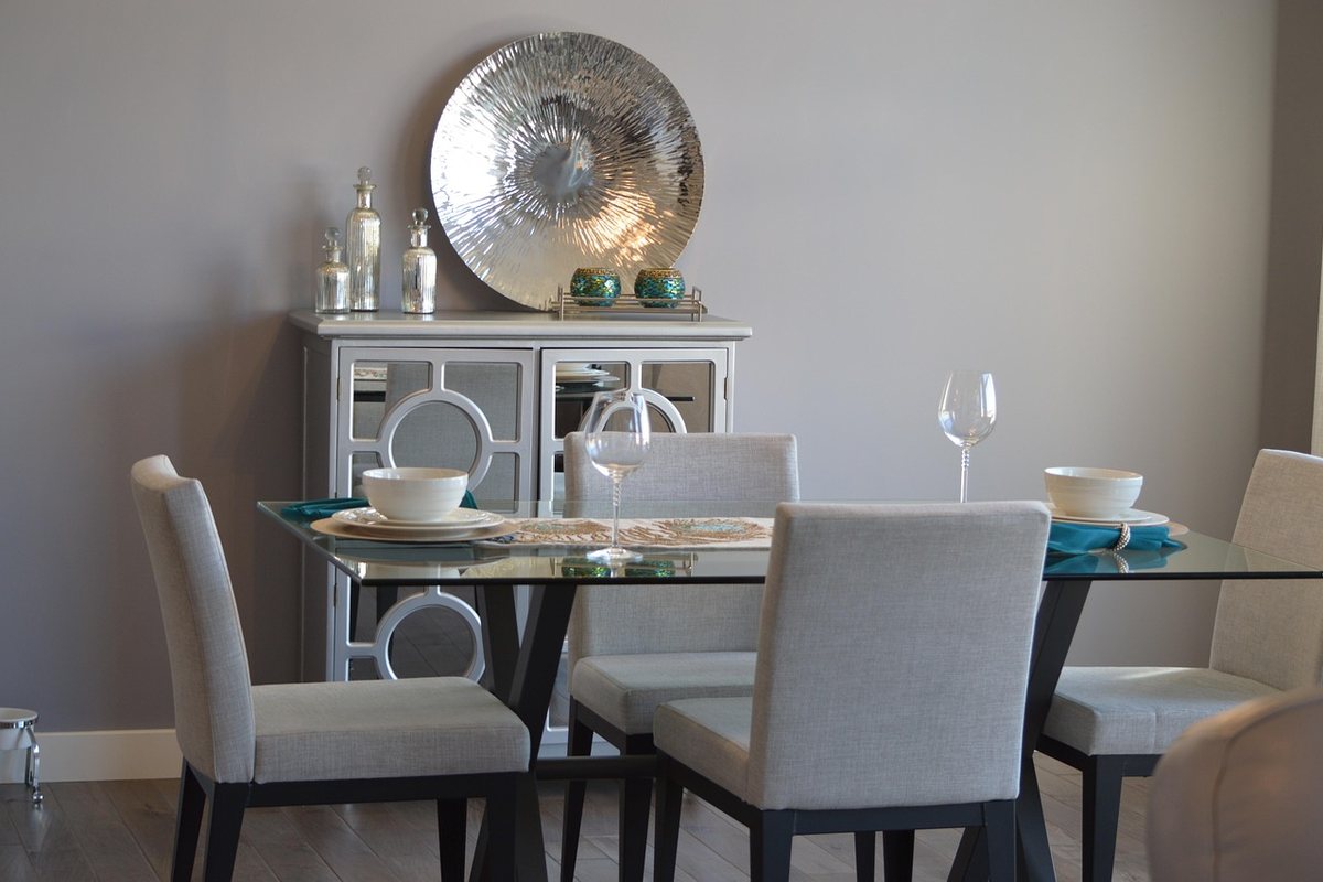 A glass dining table with six grey upholstered chairs in front of a display cabinet.
