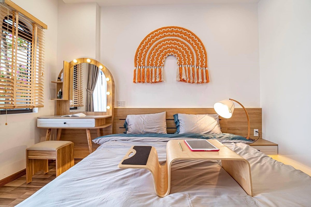 A bedroom with a wooden dressing table and a lit arched mirror against the window wall.