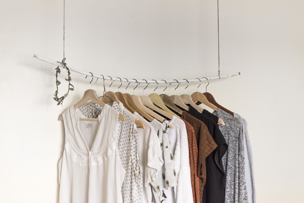 Clothes on hangers along an open rail against a white wall.