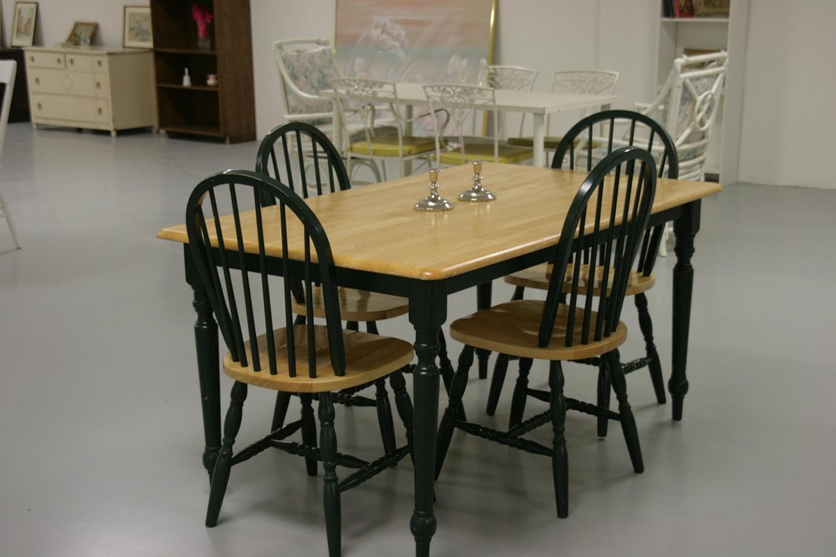 A pine-topped dining table with four dark green spindle-back chairs tucked under it.
