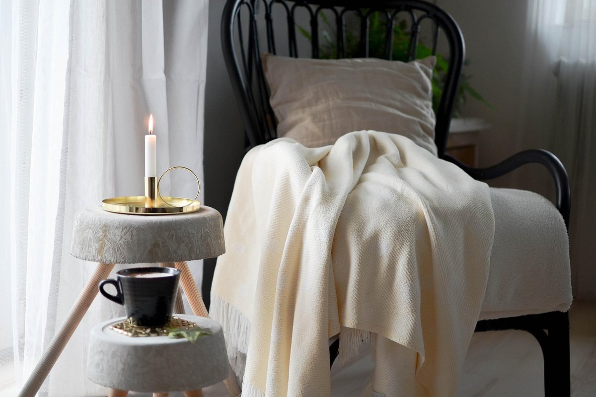 An armchair draped with a cream blanket beside a small round table holding a cup.