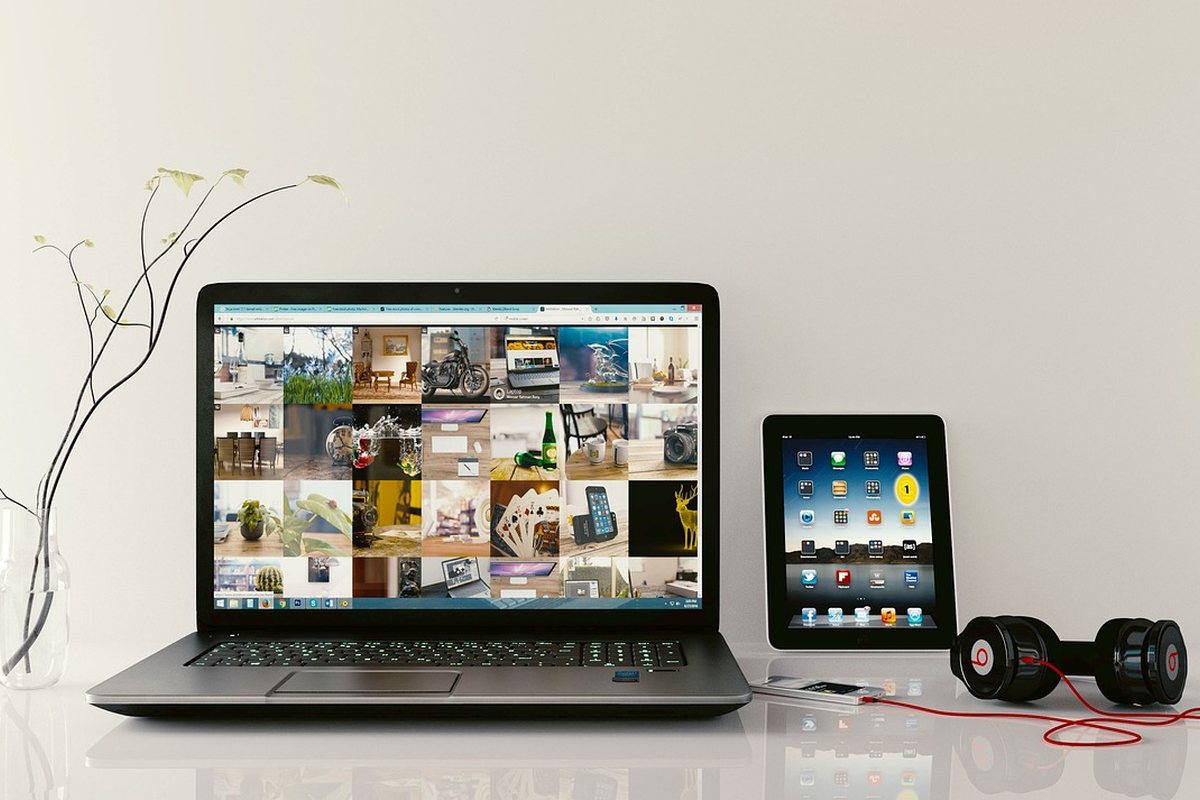 A laptop, tablet and headphones filling most of a small desk surface.