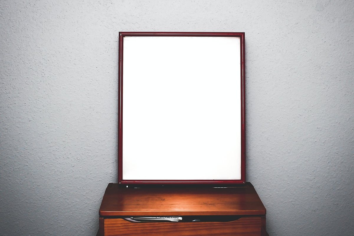 A dark wood dressing chest against a grey wall with a tall framed mirror standing on it.
