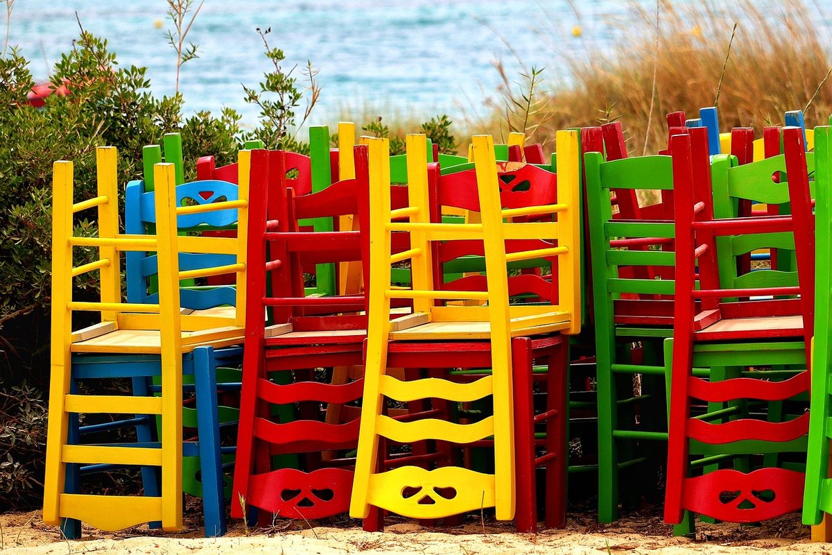 Stacks of red, yellow, green and blue wooden chairs standing by the sea.
