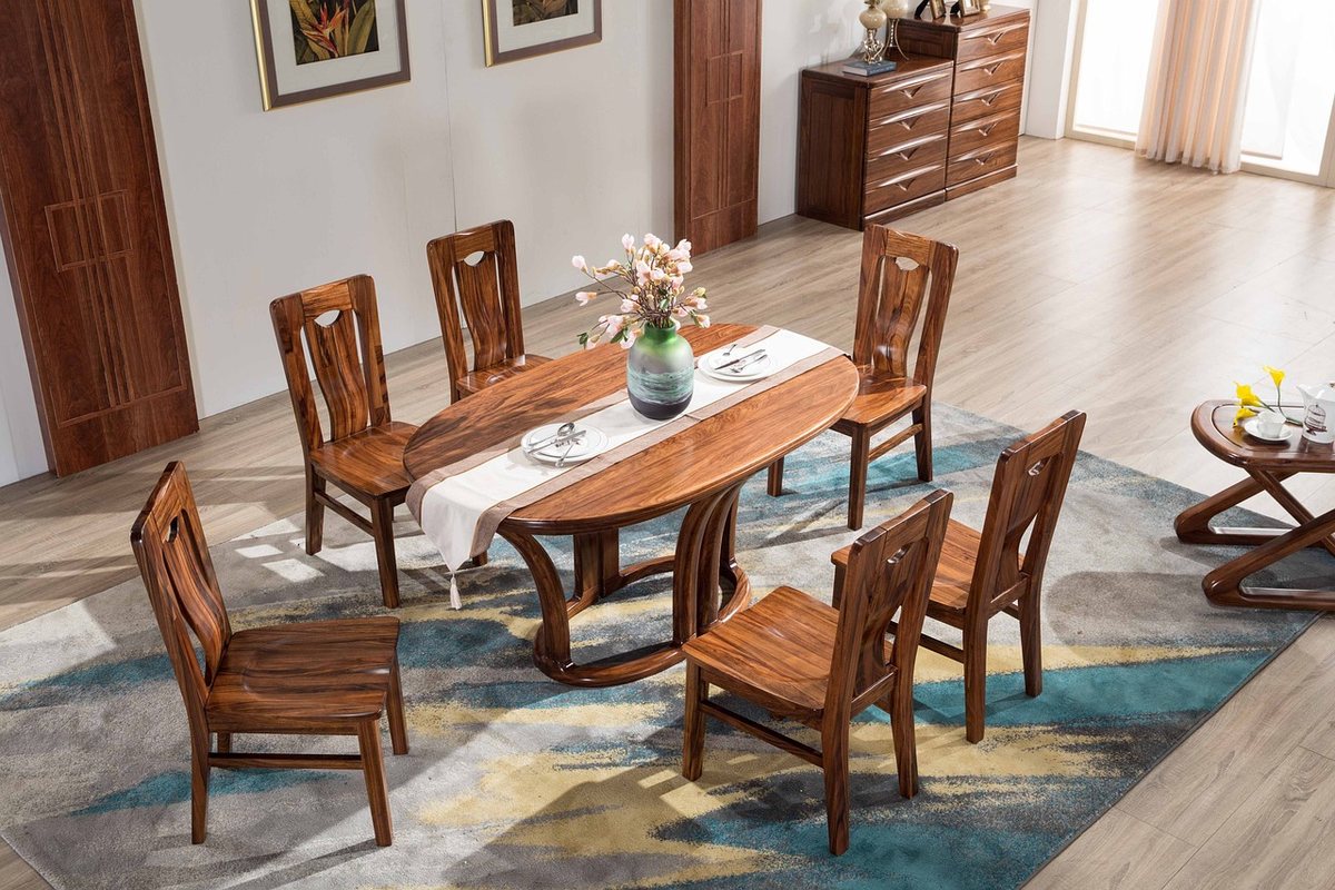 A solid wood dining table with six carved wooden chairs standing on a blue patterned rug.
