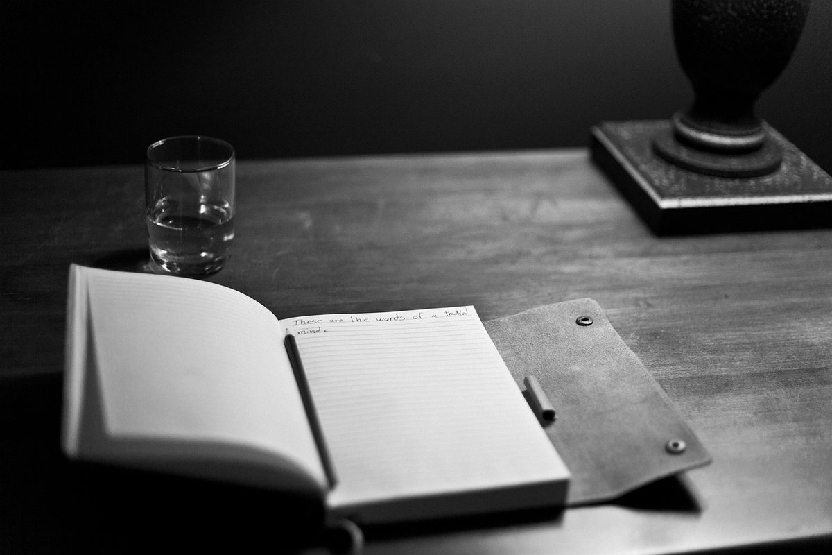 An open notebook and pen on a dark writing desk.